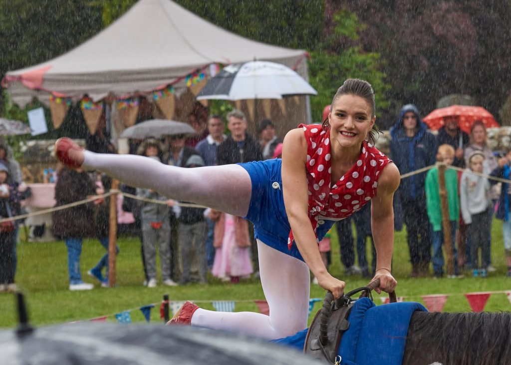 lady on horse balancing one knee on saddle one leg up in the air and smiling